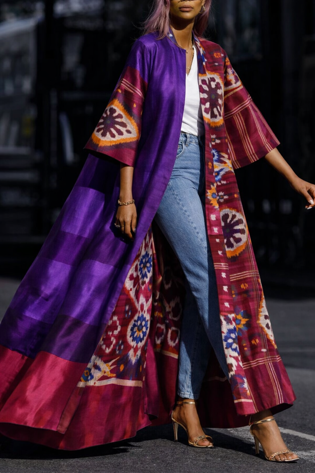 A woman wearing a long, open-front kimono-style coat with a purple satin upper section and a burgundy patterned lower section, styled over a white top and blue jeans.
